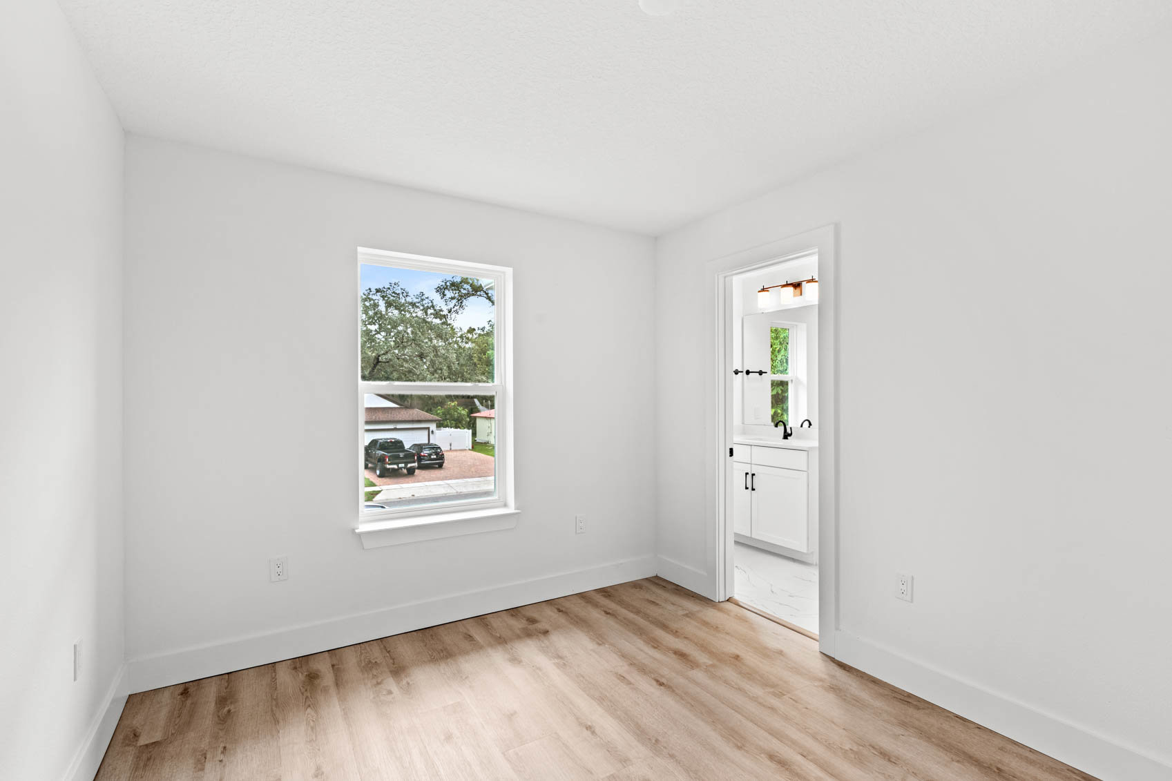 bedroom with white walls and wooden floors with bathroom door